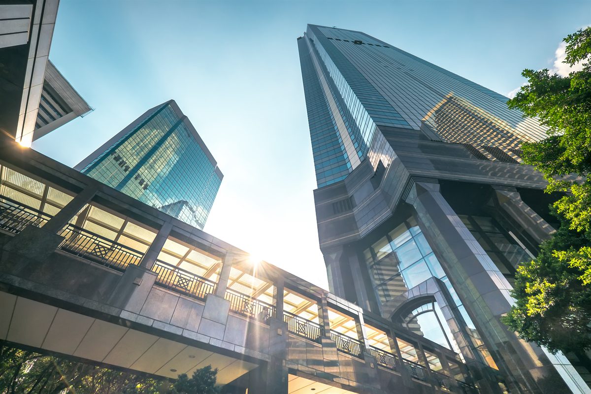 Glass office towers linked by a skybridge, seen from below